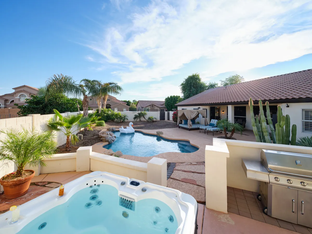 An inviting backyard scene with a pool, jacuzzi (heated spa), lounging area, grill, and lush landscaping. The scene glows with sunset light, emphasizing spaces for swimming, relaxing in the spa, and group gatherings.