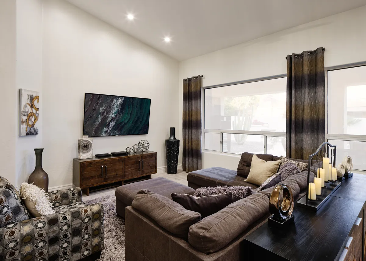A spacious, contemporary living room furnished with a large sectional sofa arranged for group gatherings. The room features a wall-mounted TV, decorative candles on the central table, modern artwork, and a stylish vase on a side table, creating a cozy yet sophisticated environment for relaxation and socializing.