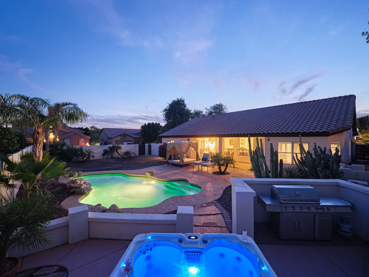 A tranquil outdoor scene showing a sparkling pool, inviting hot tub, comfortable seating area, and well-maintained landscaping. The area is ideal for relaxation and socializing after a productive workday, and the hot tub offers a soothing escape.