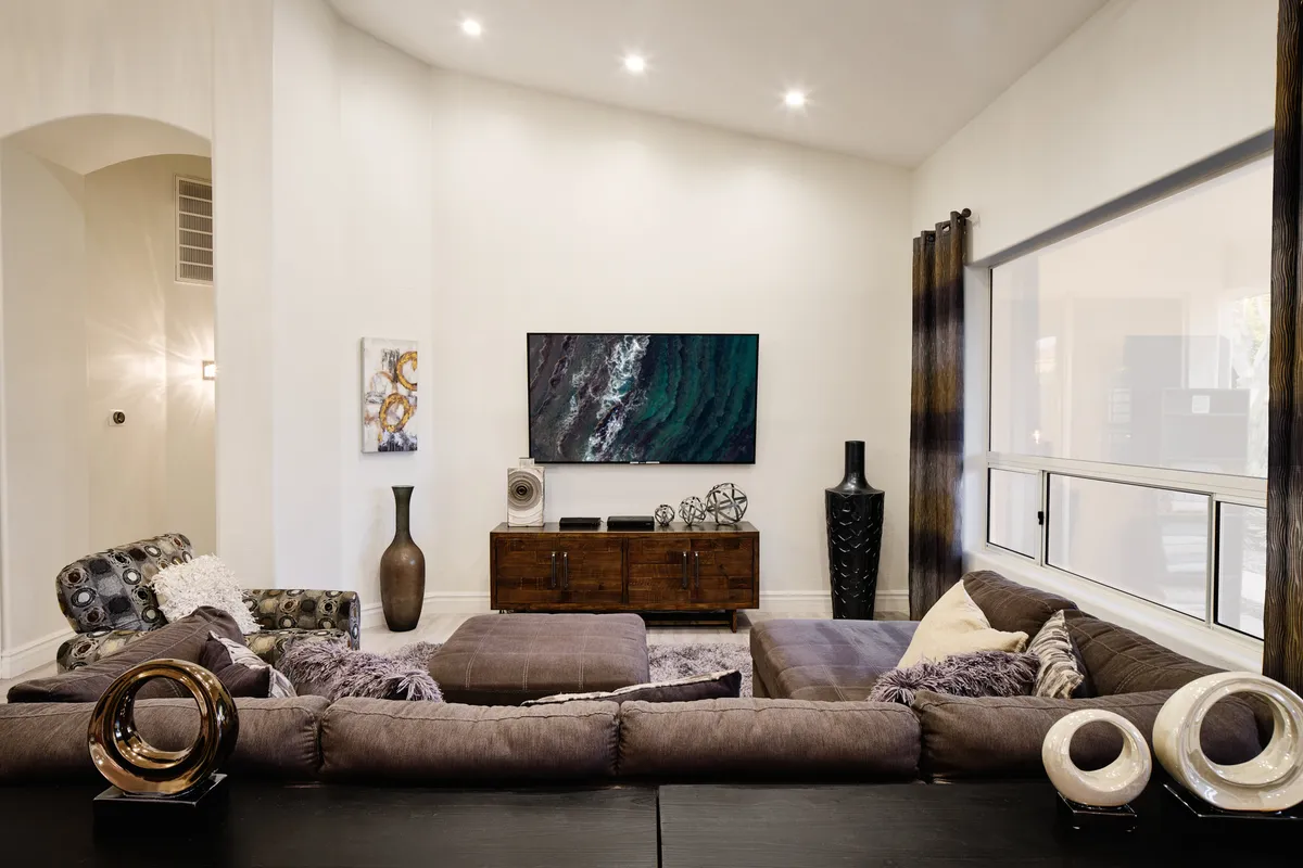 A stylish living space with a large sectional sofa, modern artwork, a TV unit with decorative items, and a tall vase, arranged for comfort and group gatherings. The setup encourages conversation, TV viewing, and relaxation.