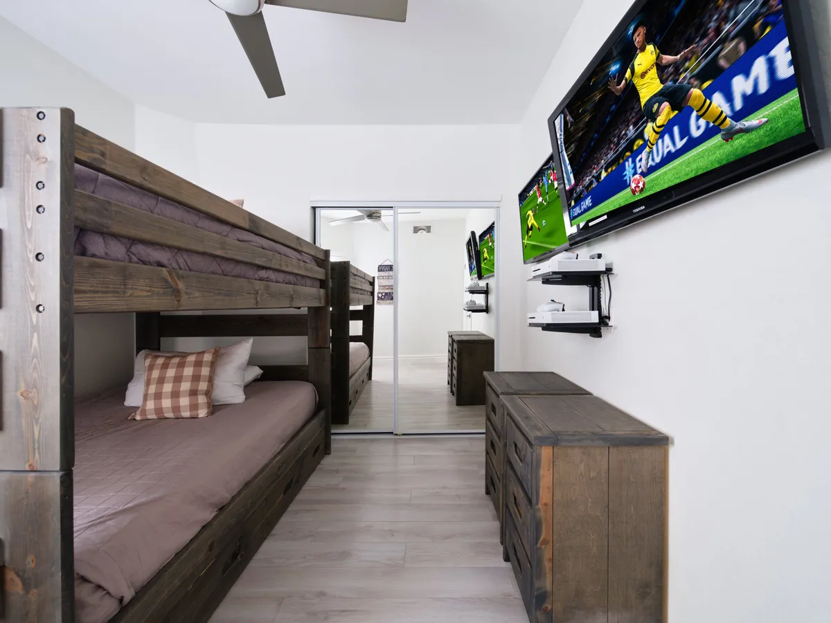 A playful bunk room with full-sized bunk beds, two television screens, a spacious dresser, and plenty of room for activities. The space feels energetic and ready for gaming, movie nights, or sleepovers, catering especially to younger guests or groups.