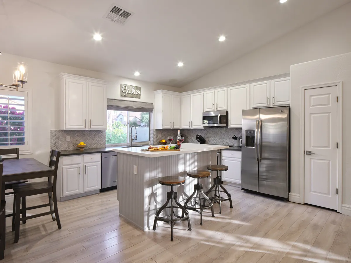 This image showcases a modern kitchen with a central island, bar stools, and prominent kitchen appliances. A 'gather' sign above the island evokes a sense of community and togetherness. The warm lighting and open design emphasize the inviting atmosphere for both casual meals and social gatherings.