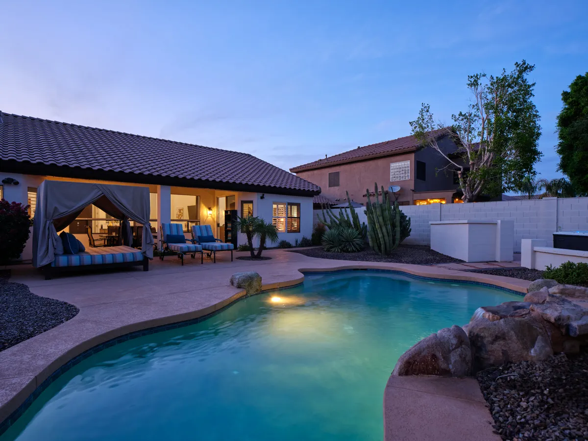 This exterior image features a tranquil swimming pool surrounded by loungers, an outdoor cabana, and thoughtful landscaping. The pool sparkles under the twilight sky, and the overall atmosphere is serene and inviting, perfect for both relaxation and social gatherings.