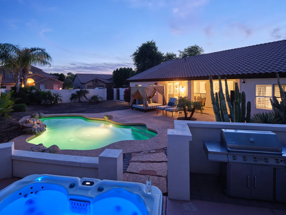 A serene and luxurious backyard scene with a sparkling swimming pool, hot tub, outdoor seating, grill area, and an inviting canopy. The area radiates relaxation and fun—ideal for swimming, barbecuing, and unwinding with the family.